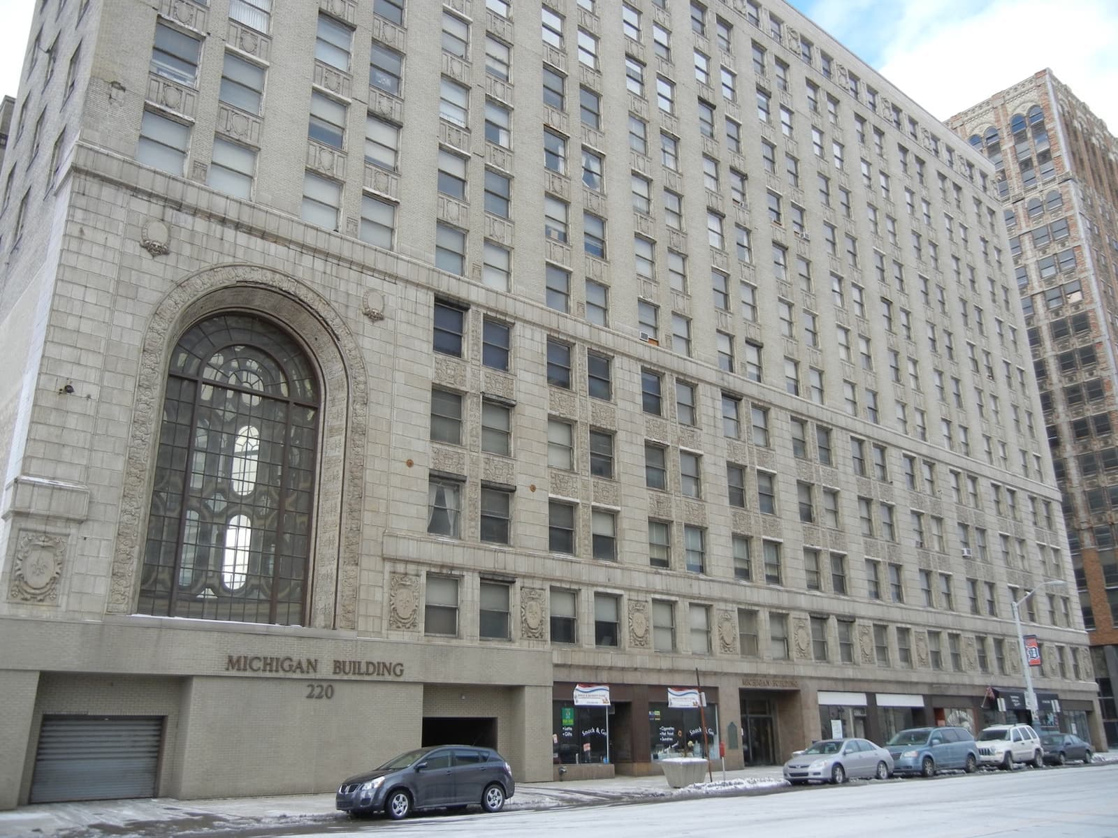 A tall pale office block with a great arched window and a street-level garage entrance