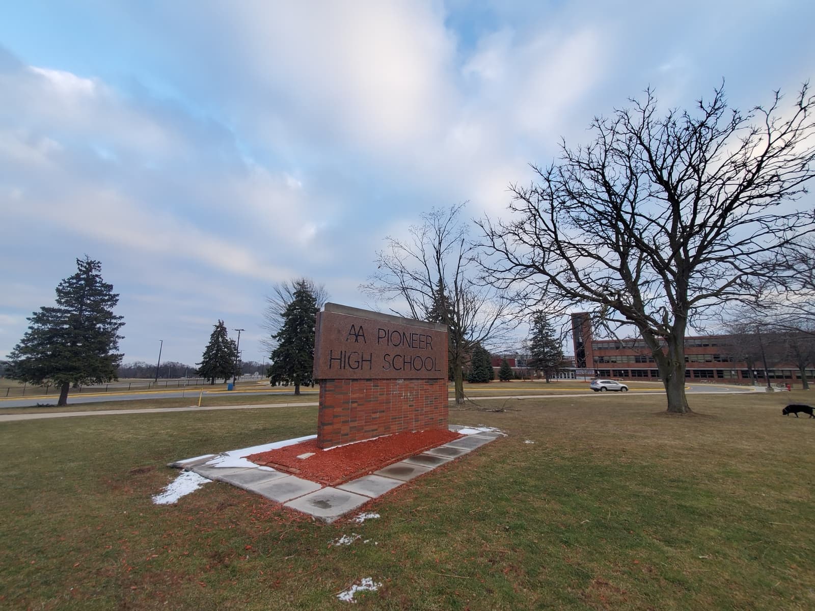 A low brick school sign on a lawn in front of Pioneer High School, bare trees and a grey sky
