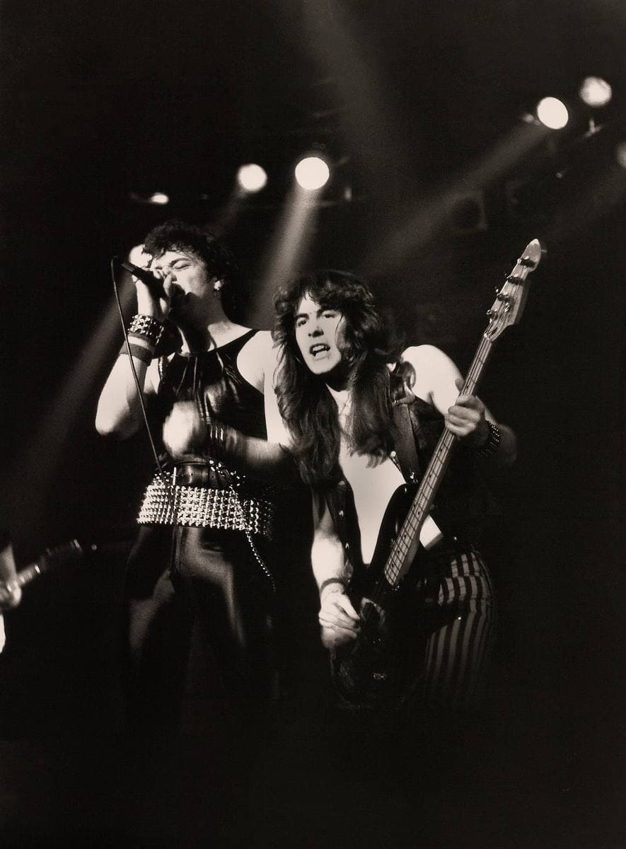 A singer and a bass player side by side under stage lights, in black and white