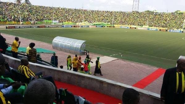 A packed stadium of fans in yellow and green around a football pitch
