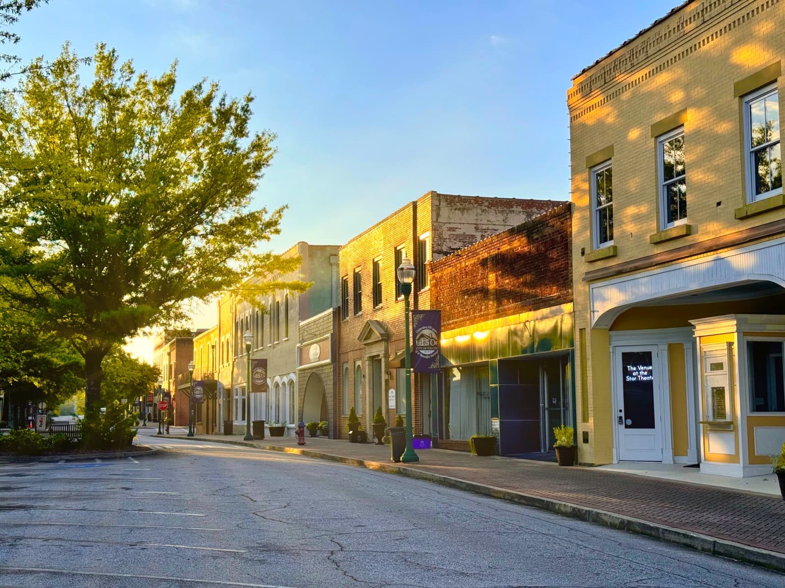 A quiet street of low painted shopfronts in early-morning light