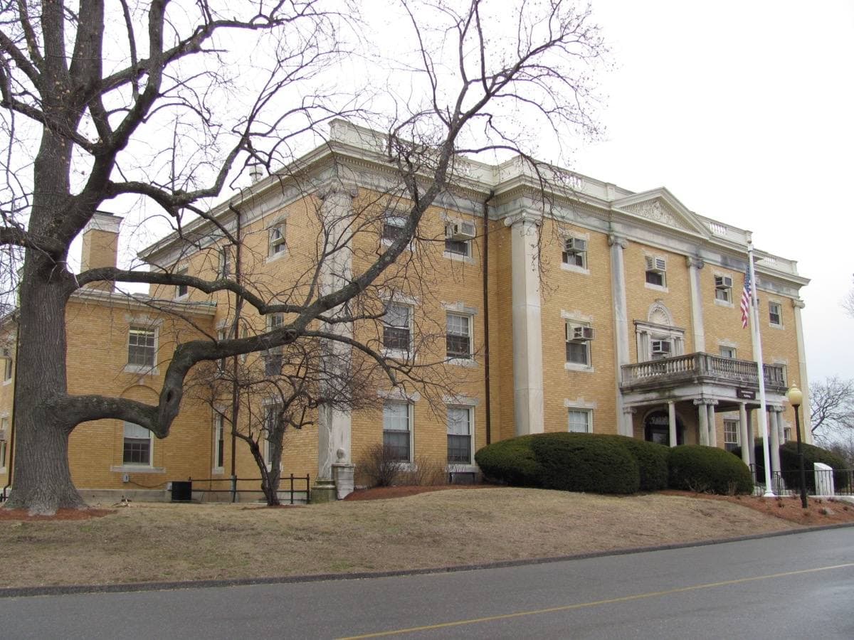 A brick hospital building with a white cupola among bare trees