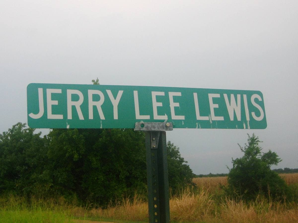 A green street sign reading Jerry Lee Lewis above a grassy field