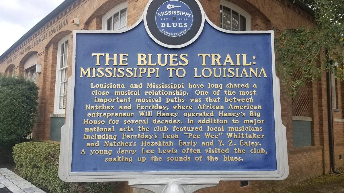 A blue roadside marker in front of a brick building