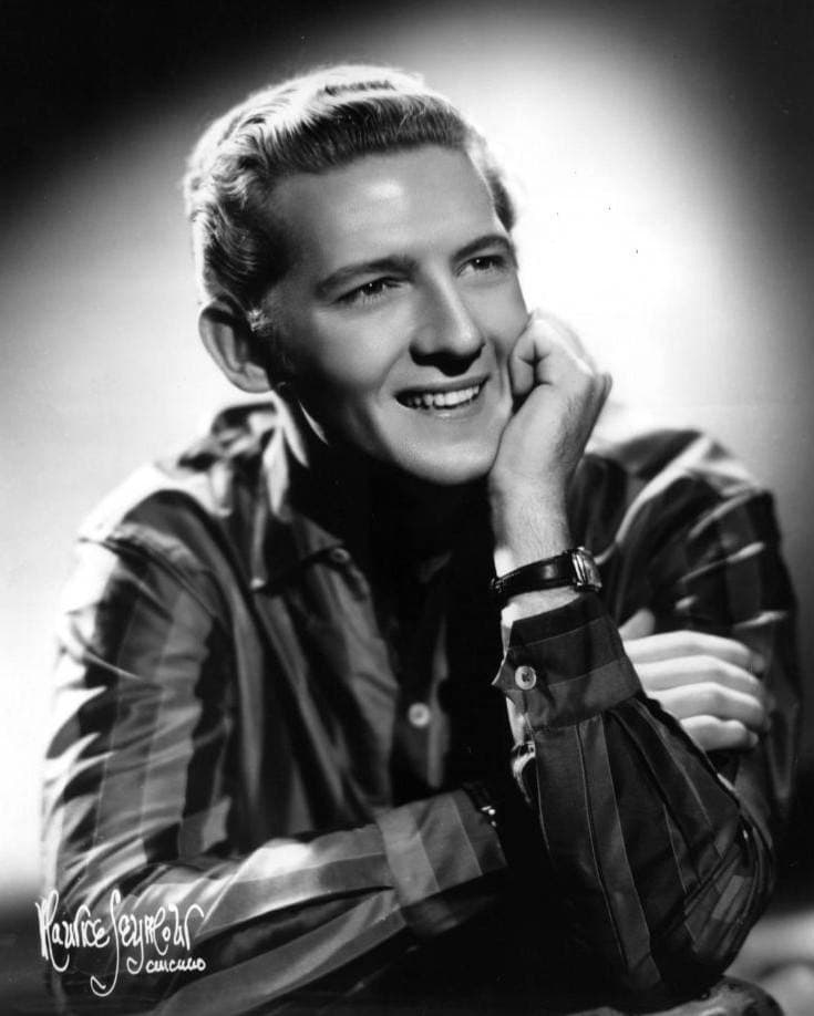 Jerry Lee Lewis smiling, chin on his hand, in a striped shirt