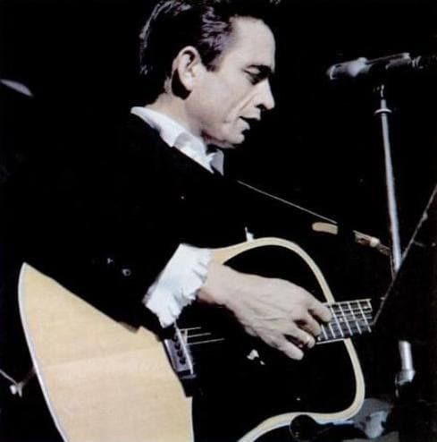 Johnny Cash in black playing an acoustic guitar at a microphone