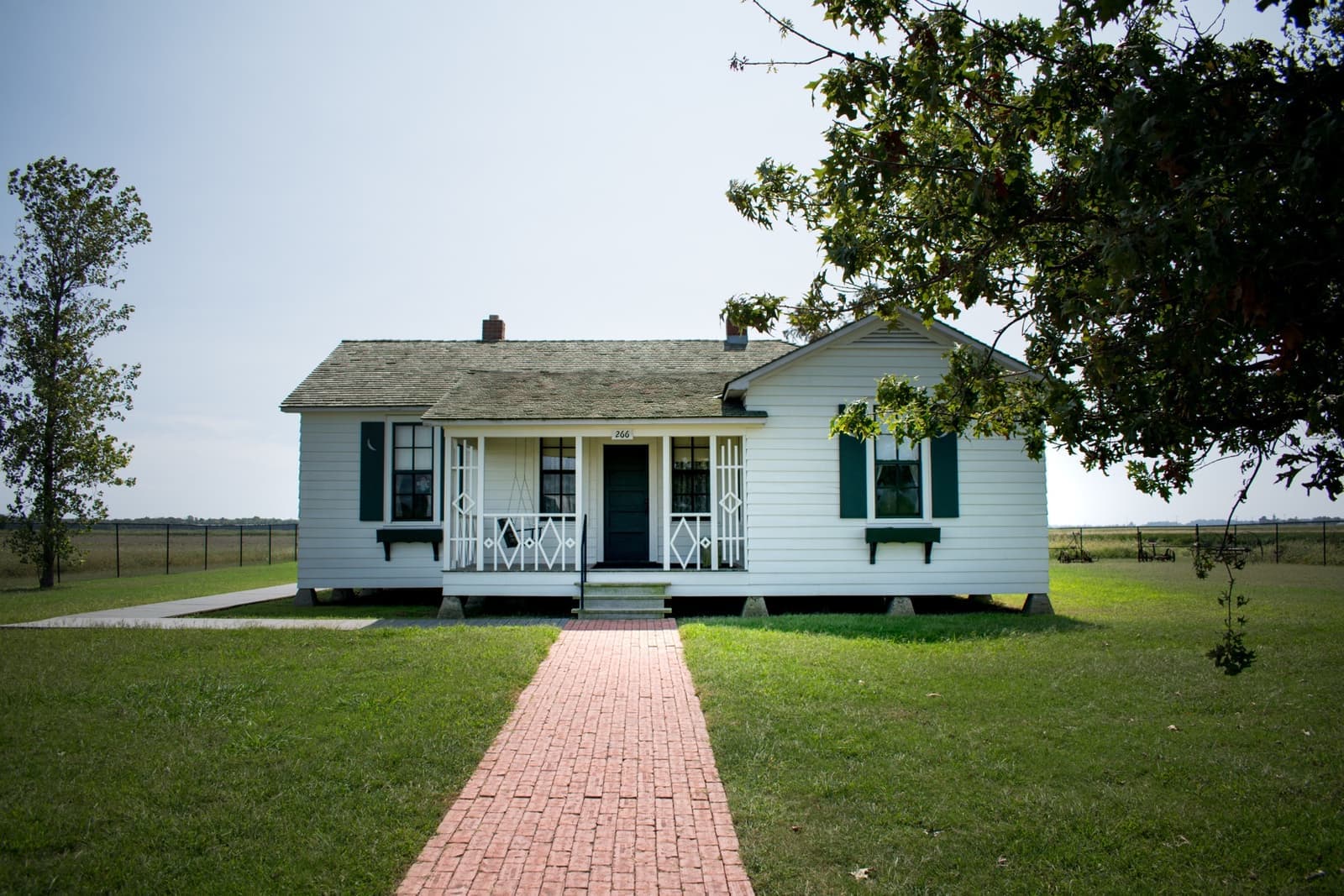 A small white farmhouse with a porch, in flat fields