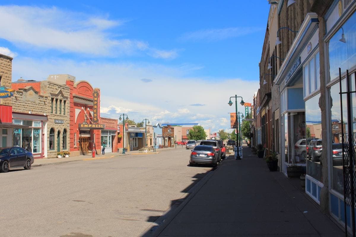 A wide prairie-town main street lined with brick and stone storefronts under a big sky