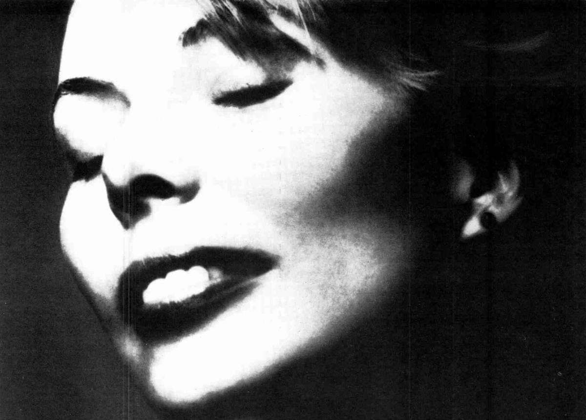 High-contrast black-and-white portrait of Joni Mitchell, smiling, her face lit from one side