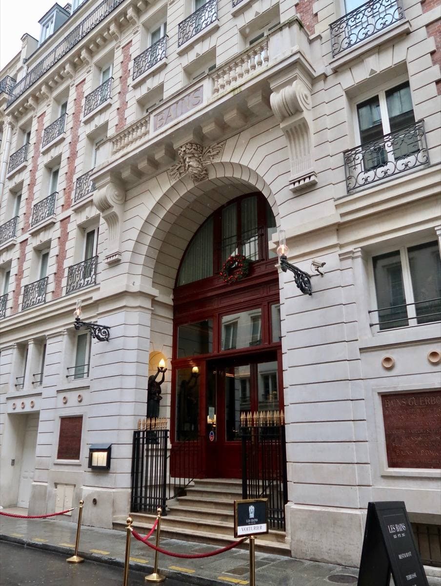 An ornate stone frontage with a tall arched doorway on a narrow Paris street