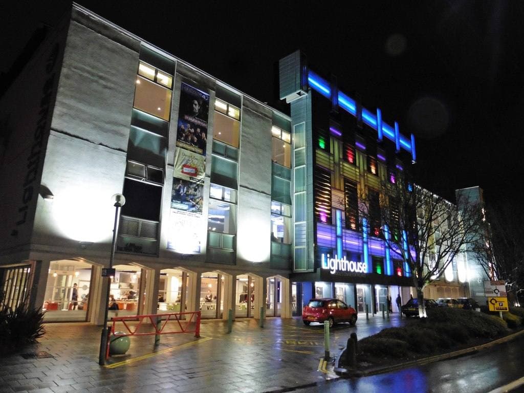 A modern arts centre at night with blue and white light strips on its front and its name on the glass