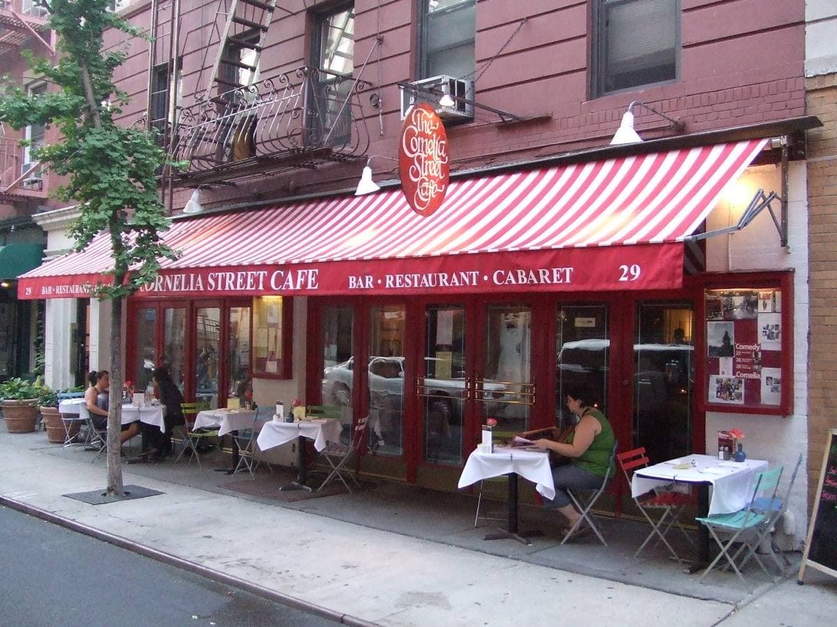 A café with a red-and-white striped awning and tables on the pavement