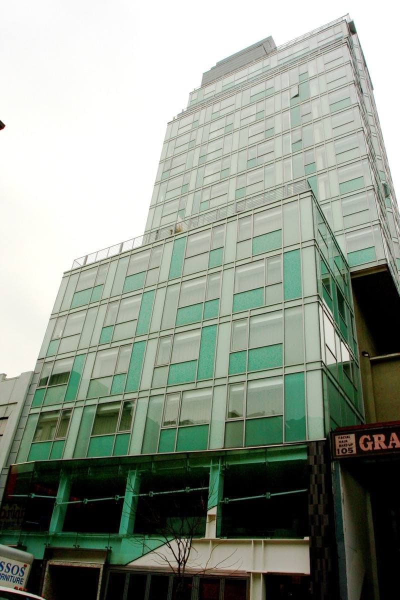 A tall glass tower with green-tinted windows above low brick buildings