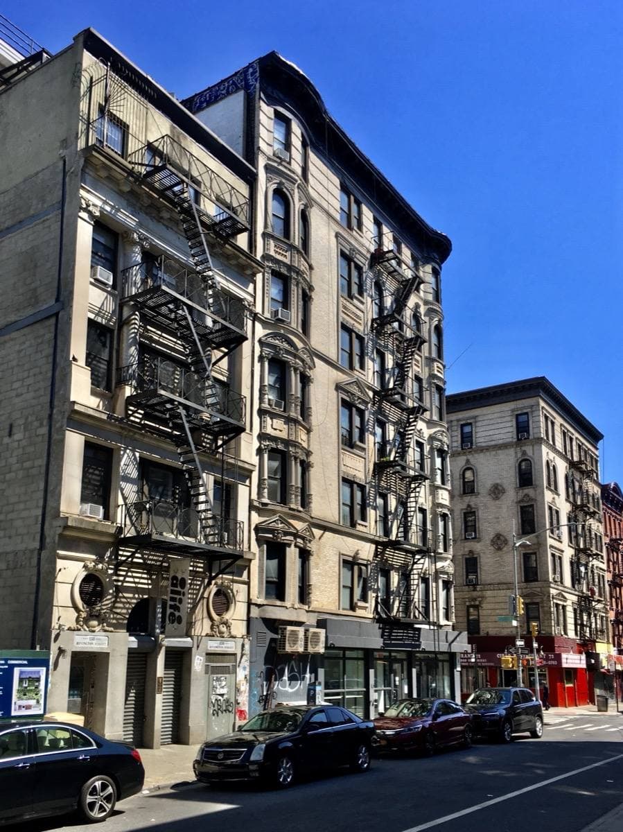 Tenement buildings with fire escapes along a sunny Lower East Side street