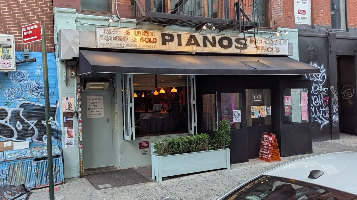 A shopfront with a black awning and a sign reading PIANOS