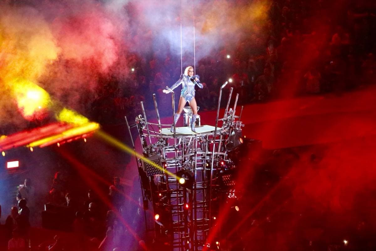 A performer on a raised lit platform in red light and smoke above a stadium floor