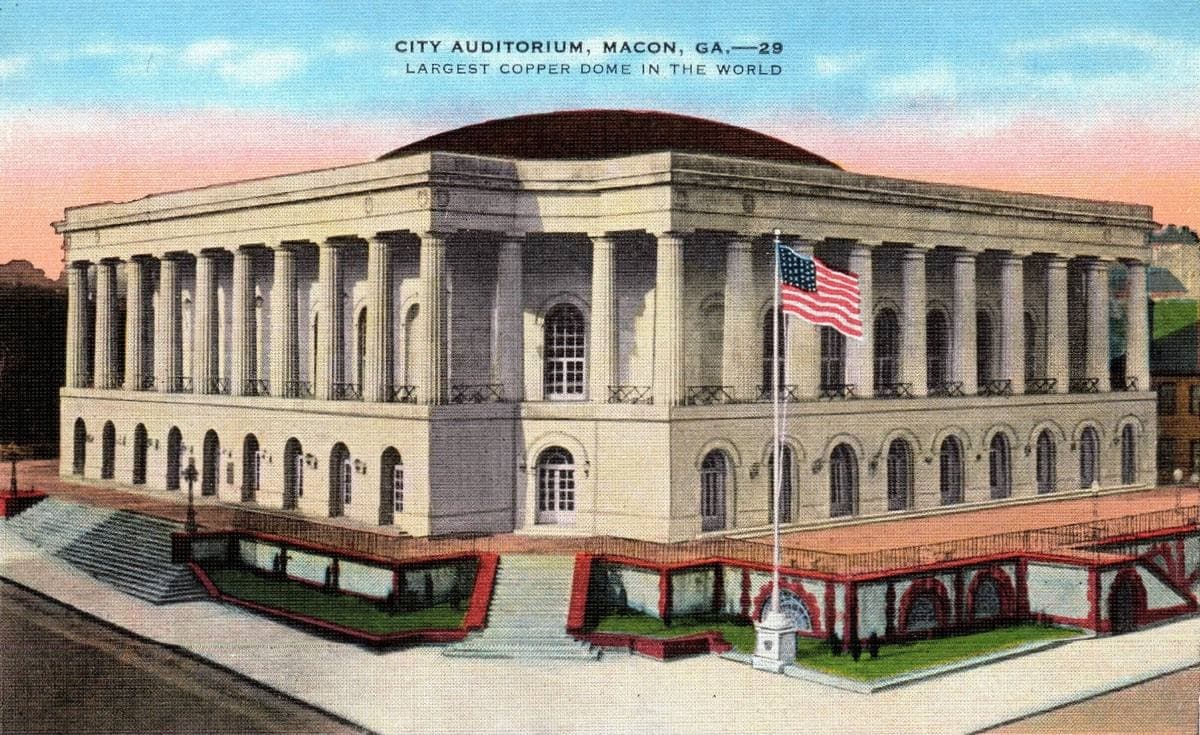 Coloured postcard of a domed, columned auditorium under a pink sky