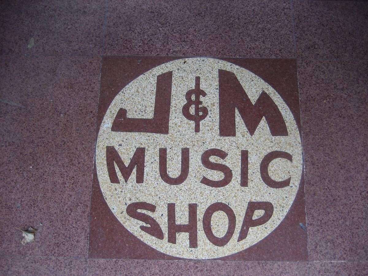A round terrazzo floor sign reading J&M Music Shop
