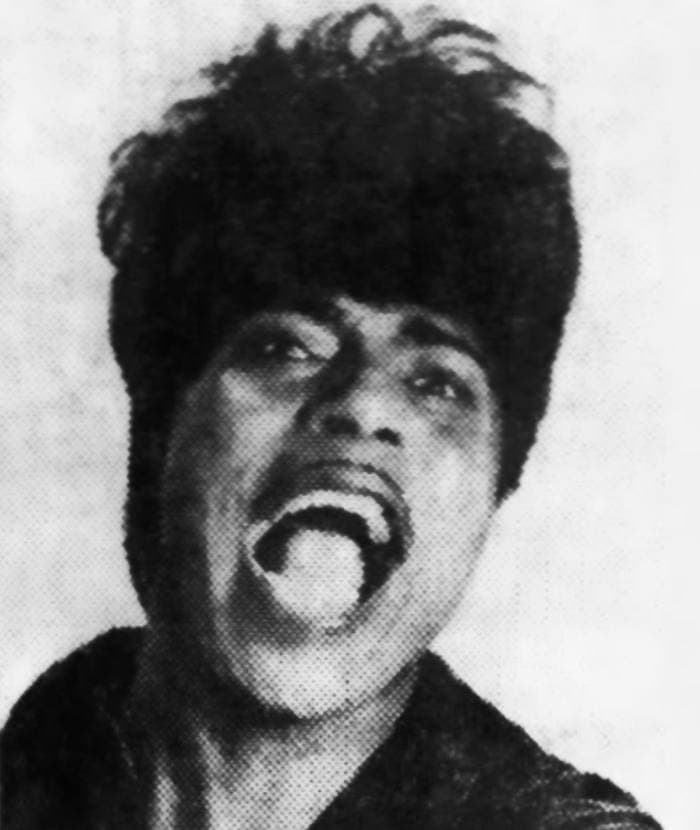 Little Richard mid-shout, mouth wide open, in a black-and-white publicity photograph