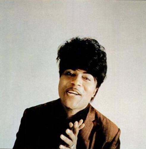 Little Richard smiling, hands together, in a dark jacket