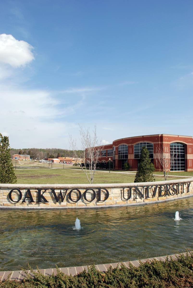 A fountain and low sign reading Oakwood University in front of campus buildings