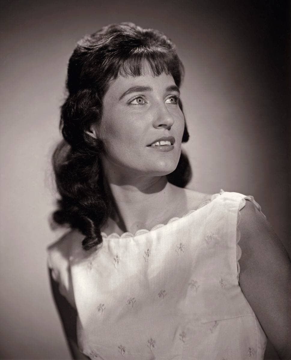 Loretta Lynn in 1962, dark hair swept up, smiling, in a light dress