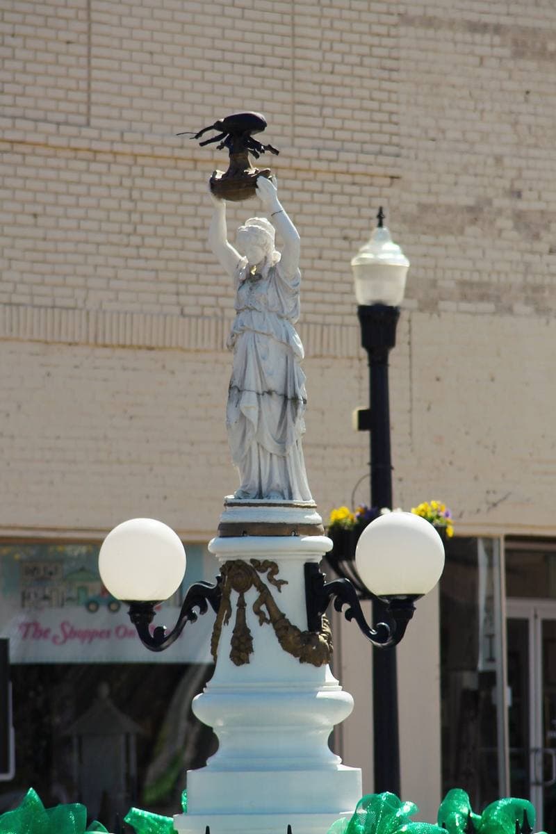 A classical statue holding up a giant boll weevil in a town square