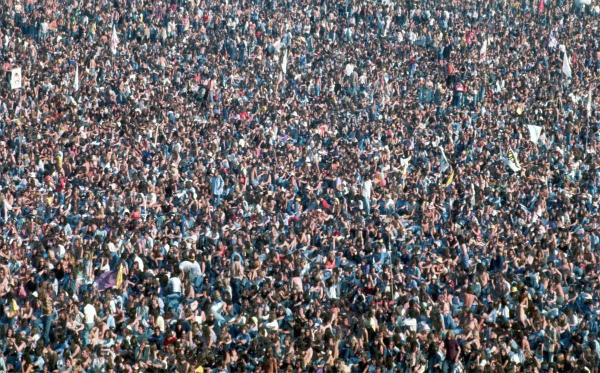 A huge crowd on a grass field in front of a distant stage