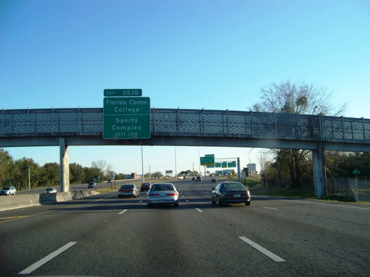 A Westside Jacksonville interstate under a footbridge with green road signs
