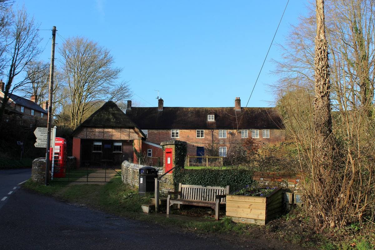 A village lane in winter sun with brick cottages, a red telephone box and a wooden bench