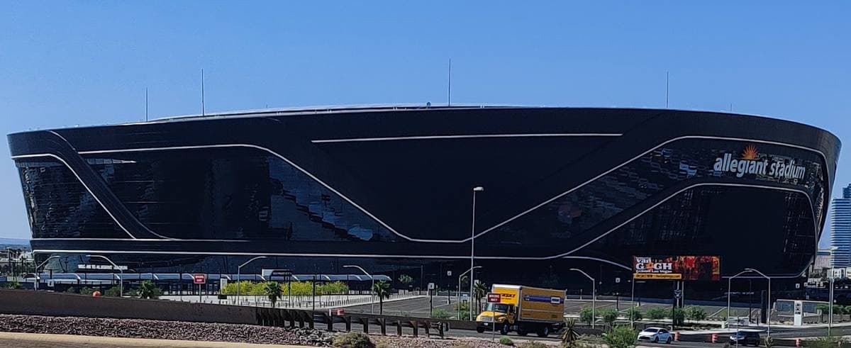 A huge black stadium with a curved white line across it, under a blue sky