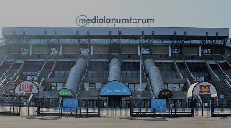 The front of a large concrete arena with the name Mediolanum Forum on its roof