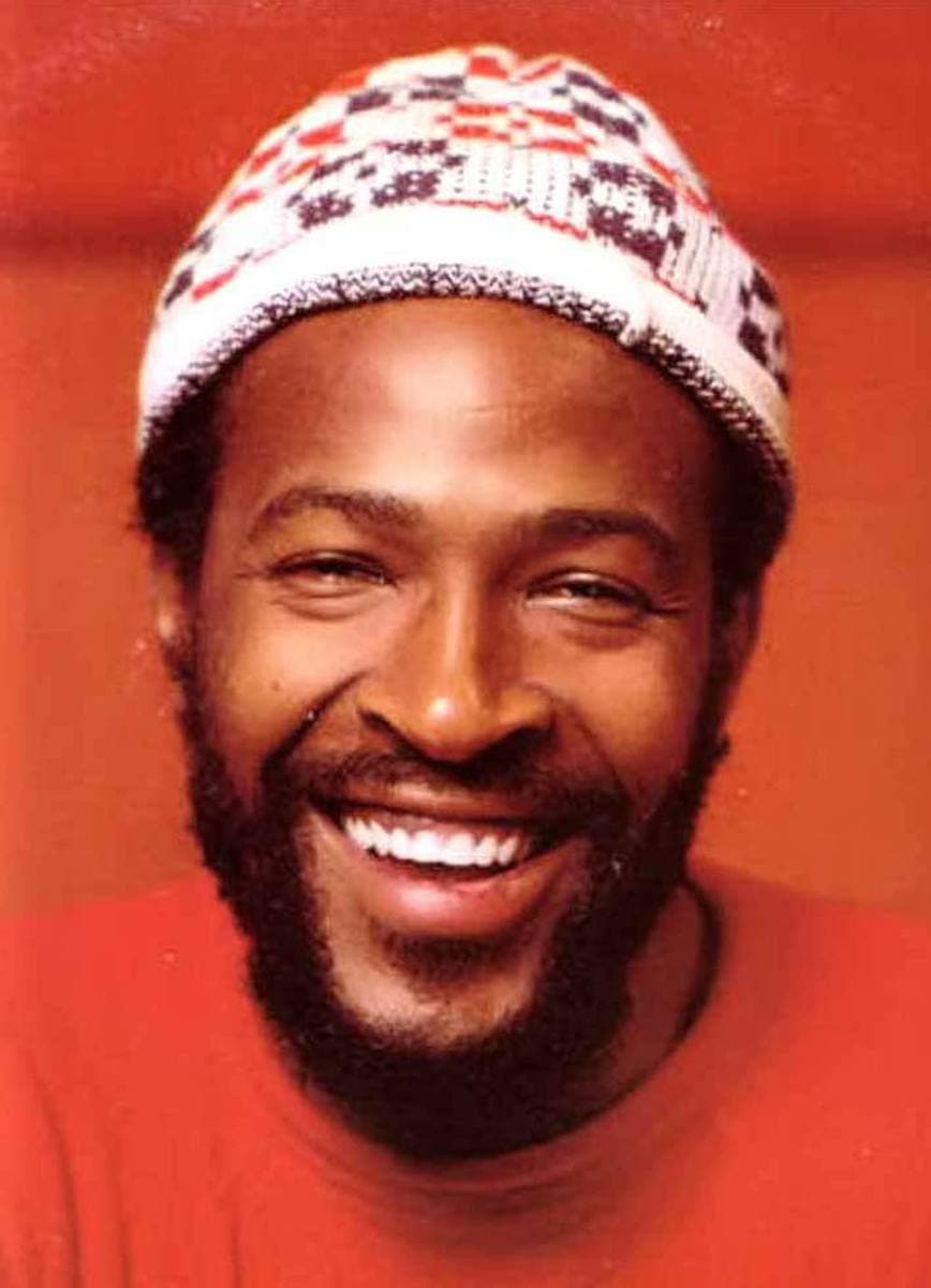 A laughing bearded man in a white and red patterned knitted cap against a red background