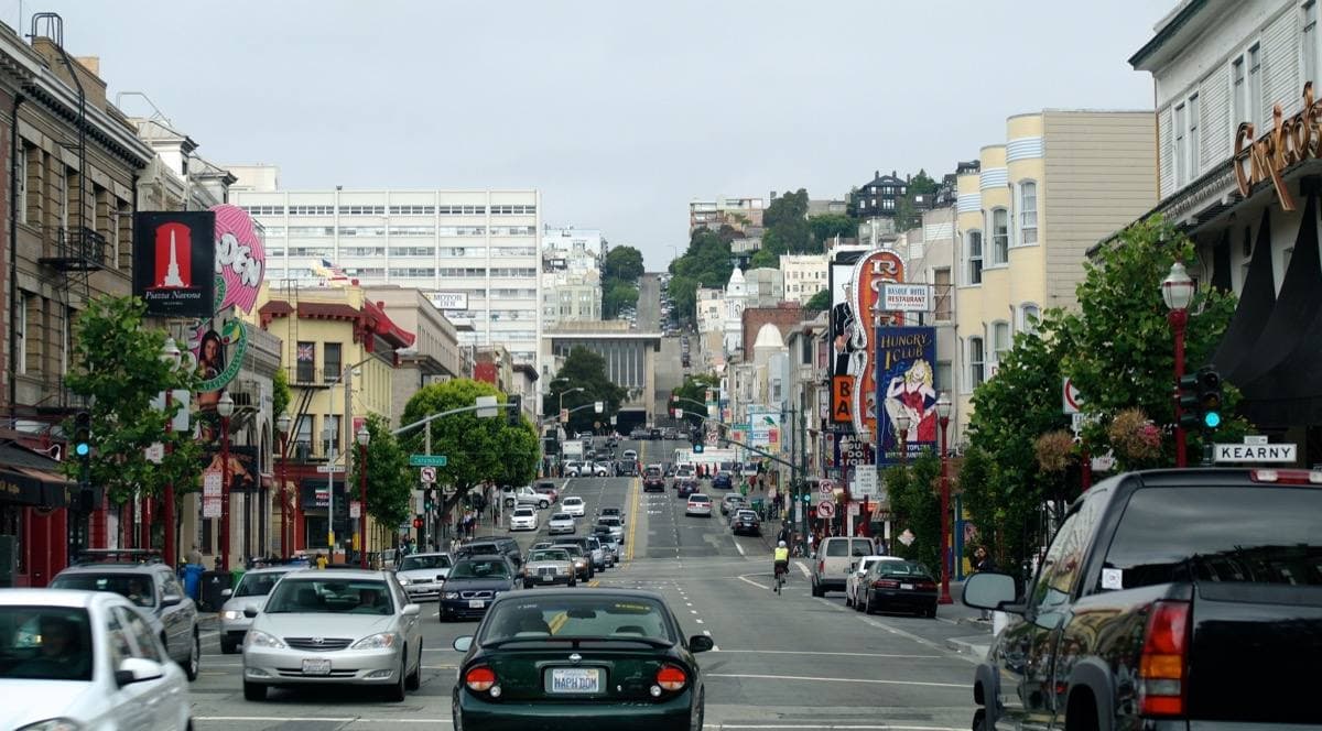 A North Beach street of club fronts and signs on a grey day