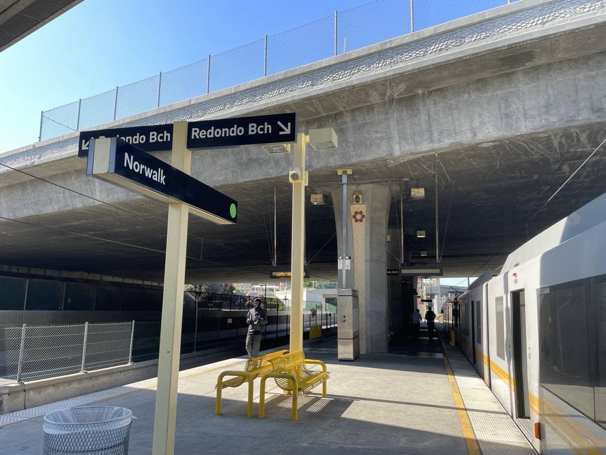 A rail platform between freeway lanes under a pale sky in Norwalk, California