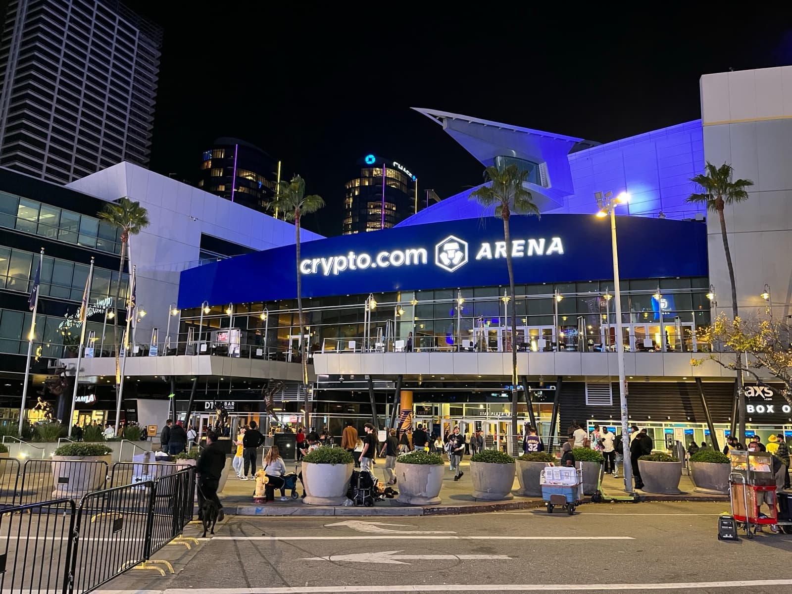 A glass arena entrance lit blue at dusk, palm trees in front
