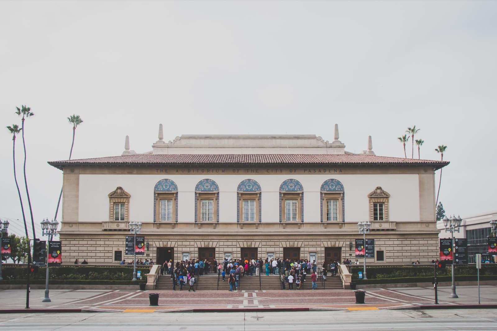 A pale Italianate auditorium front with arched windows and palms behind