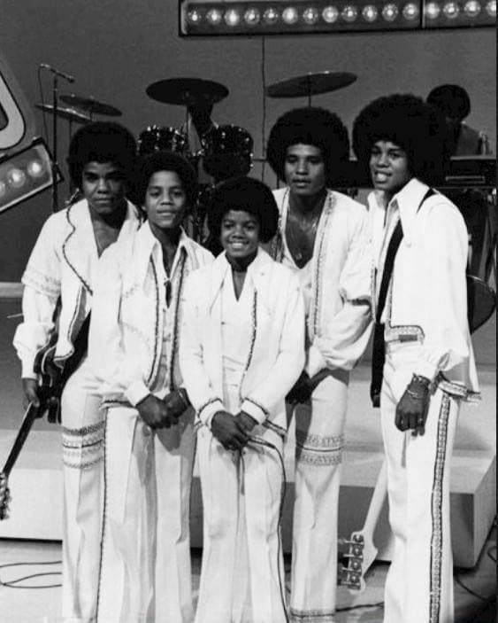 The five Jackson brothers standing together in white outfits, the young Michael in front