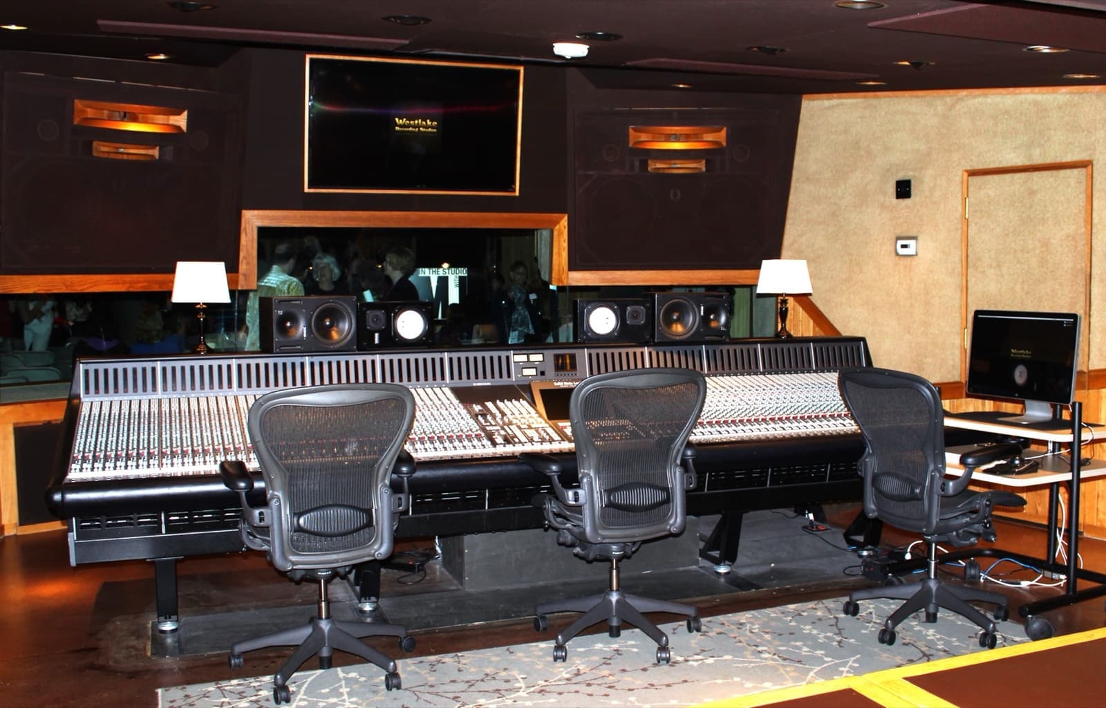 A long mixing desk with three office chairs facing studio monitors in a wood-panelled room