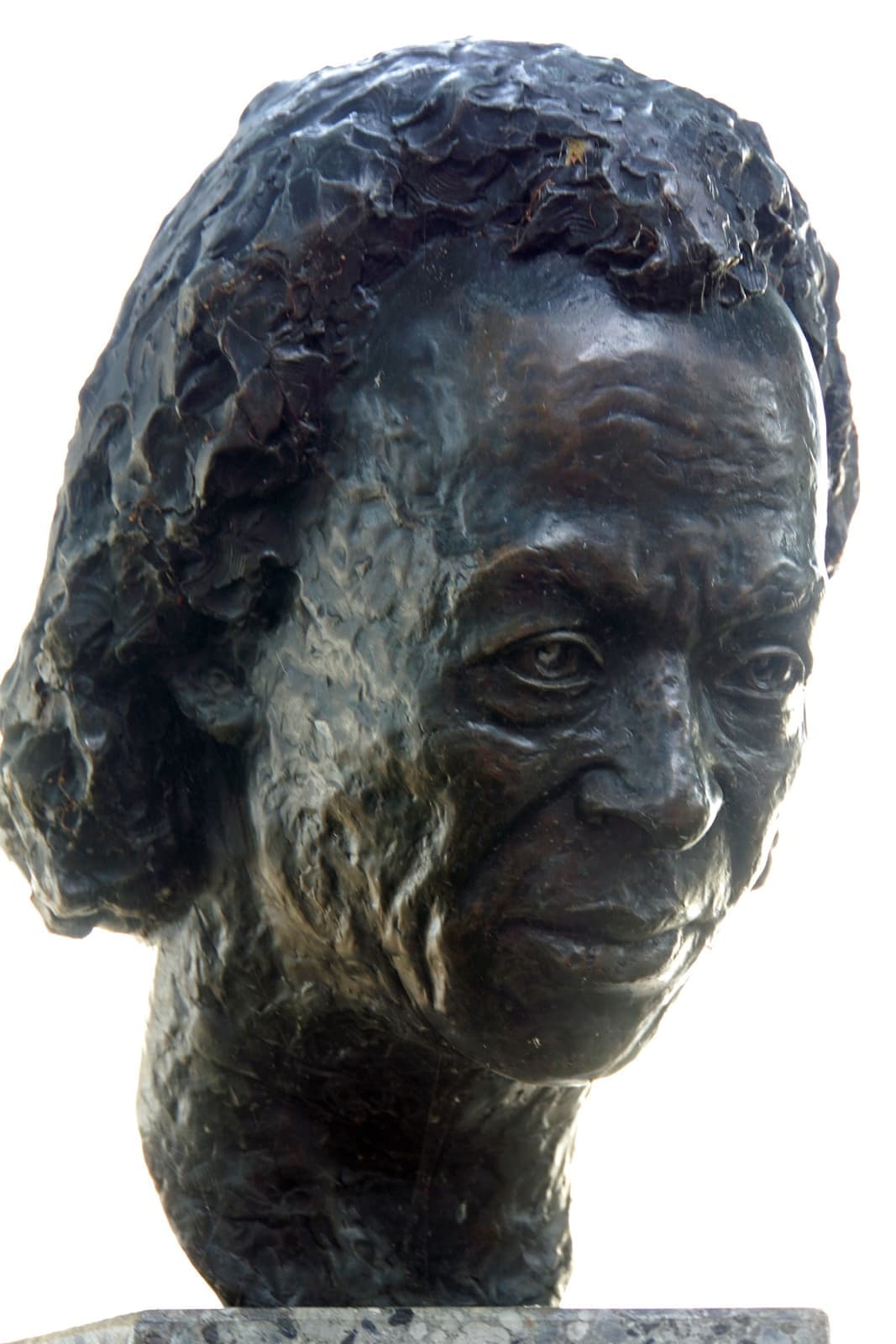 A bronze bust of an older Miles Davis with curly hair and a lined face, against a pale sky