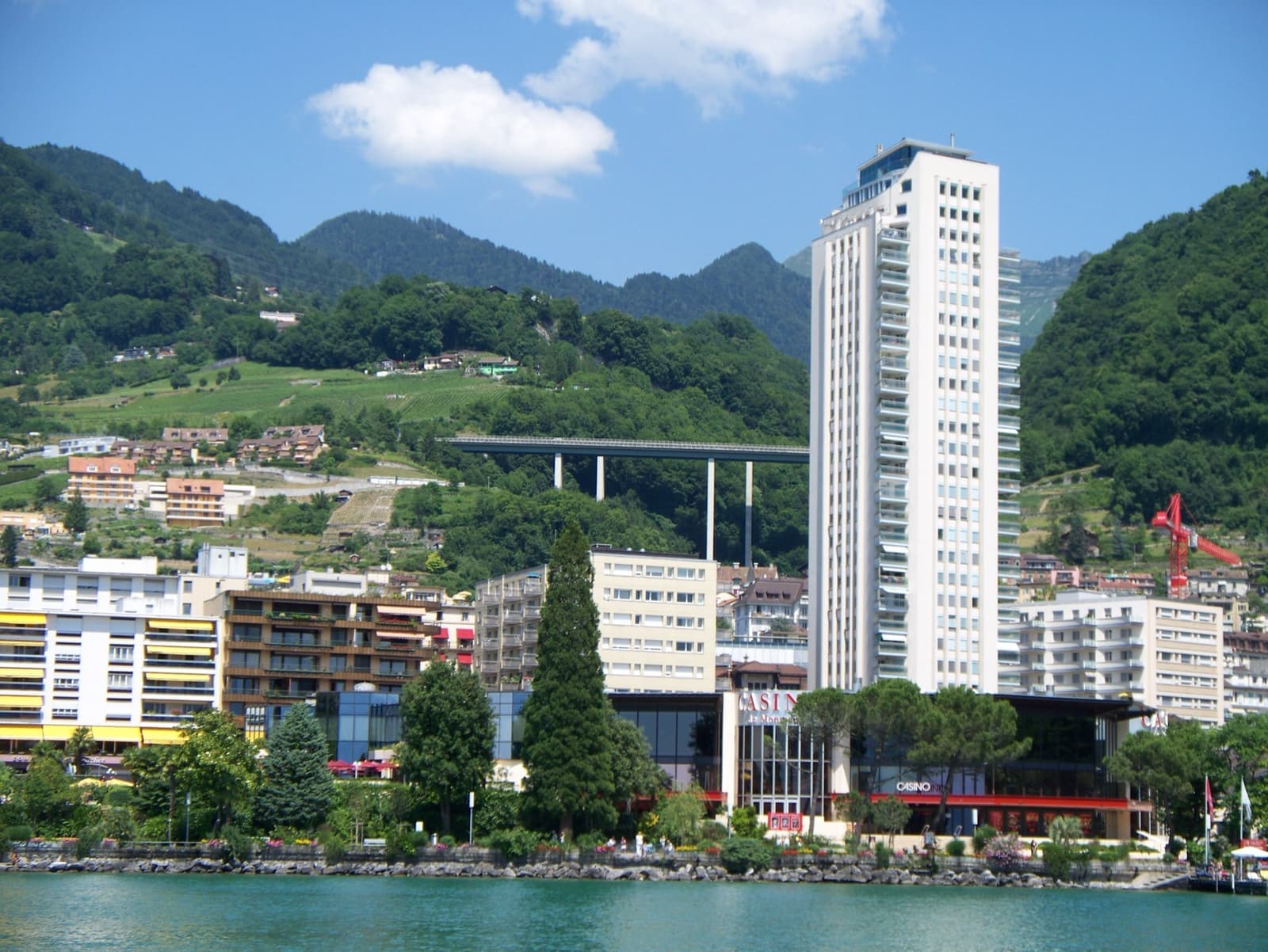The low Casino building on the Montreux lakefront below a white tower block and green mountains