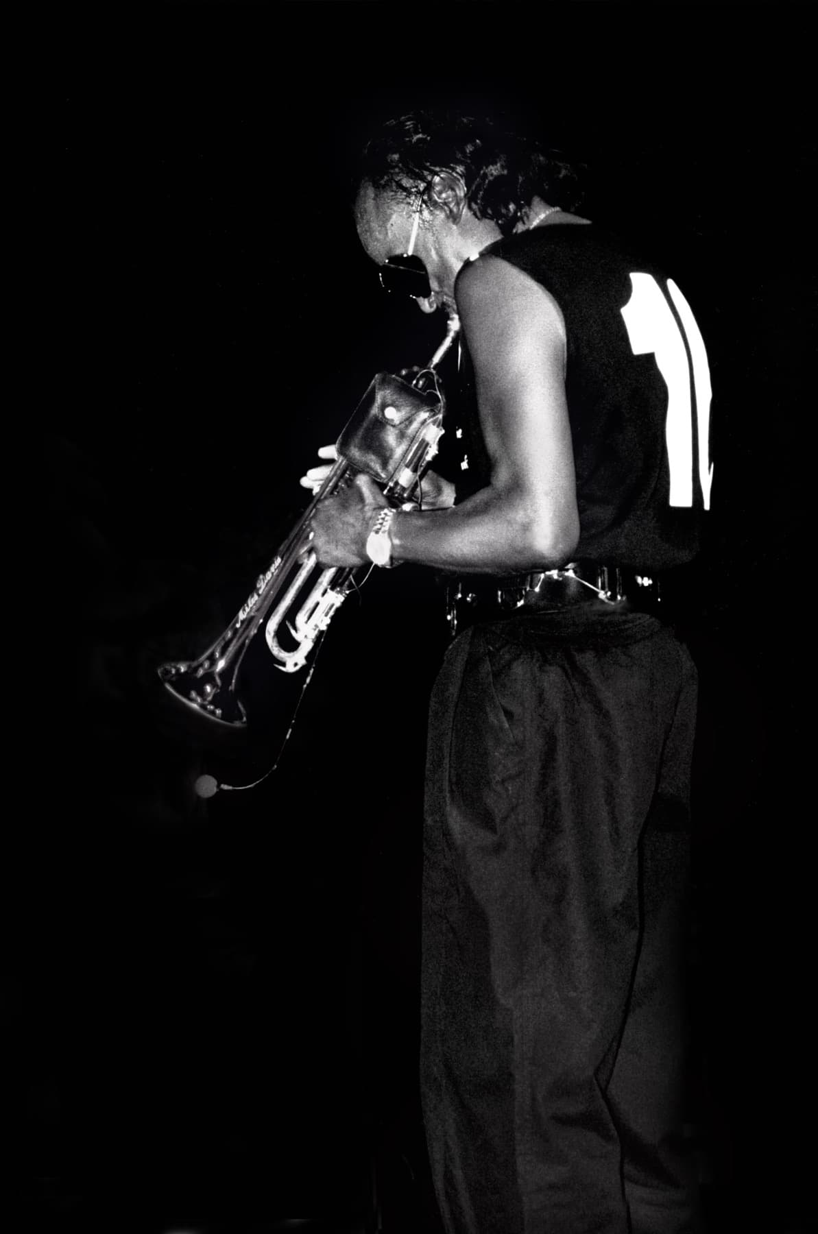 Miles Davis in silhouette against a black stage, turned half away, trumpet raised