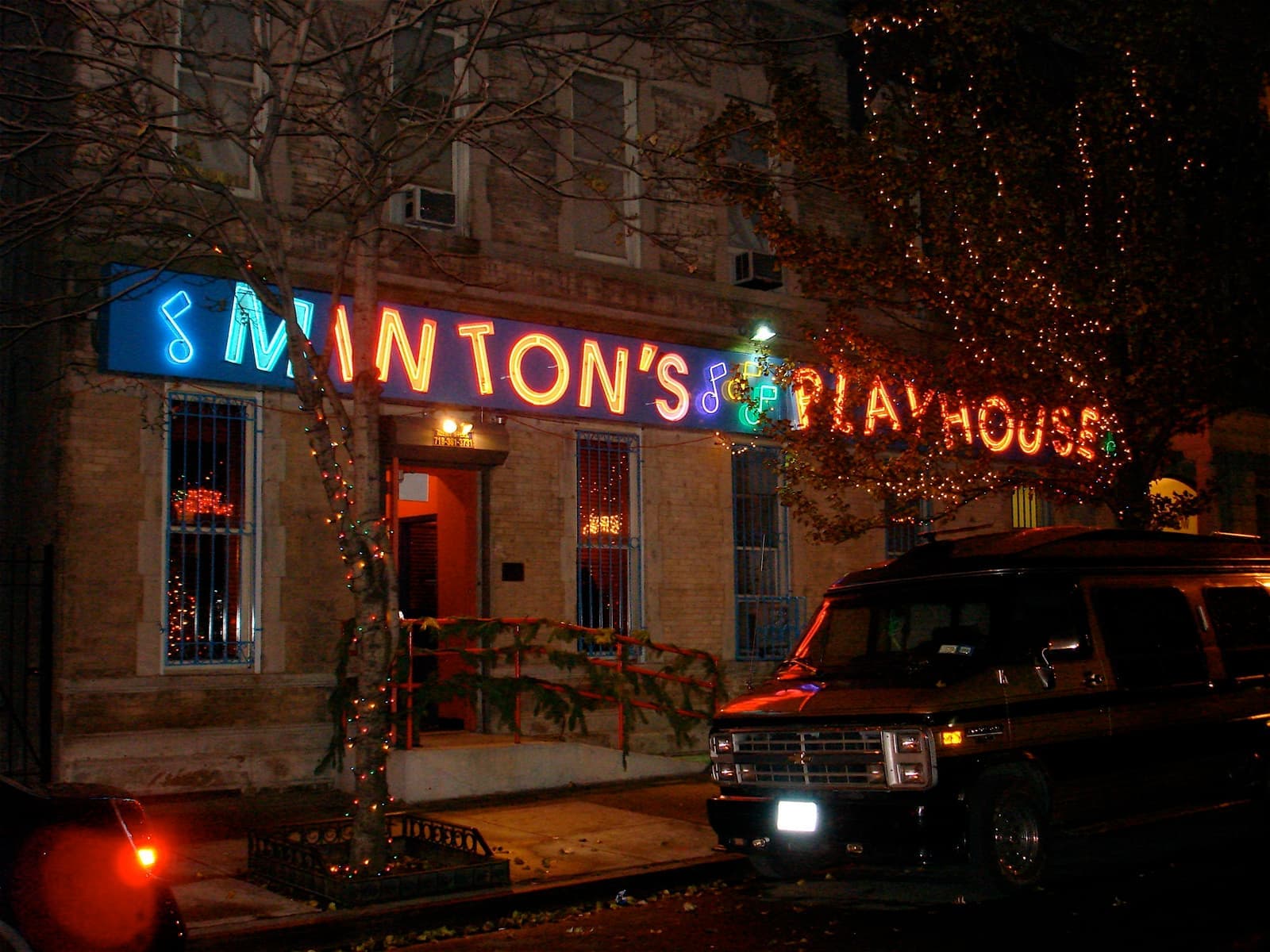 Blue and red neon spelling Minton’s Playhouse over a doorway on a Harlem street at night