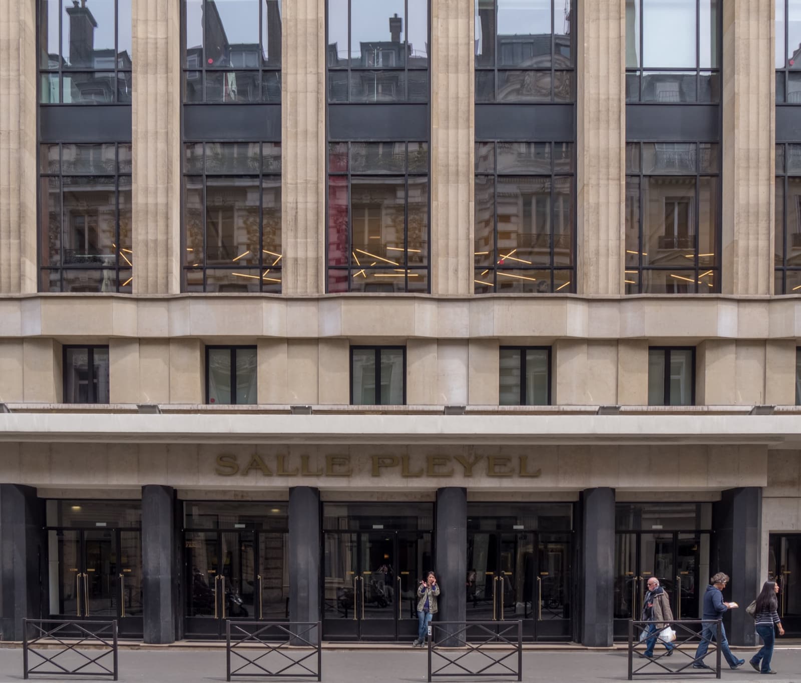 The pale stone front of the Salle Pleyel concert hall with tall windows above its glass doors