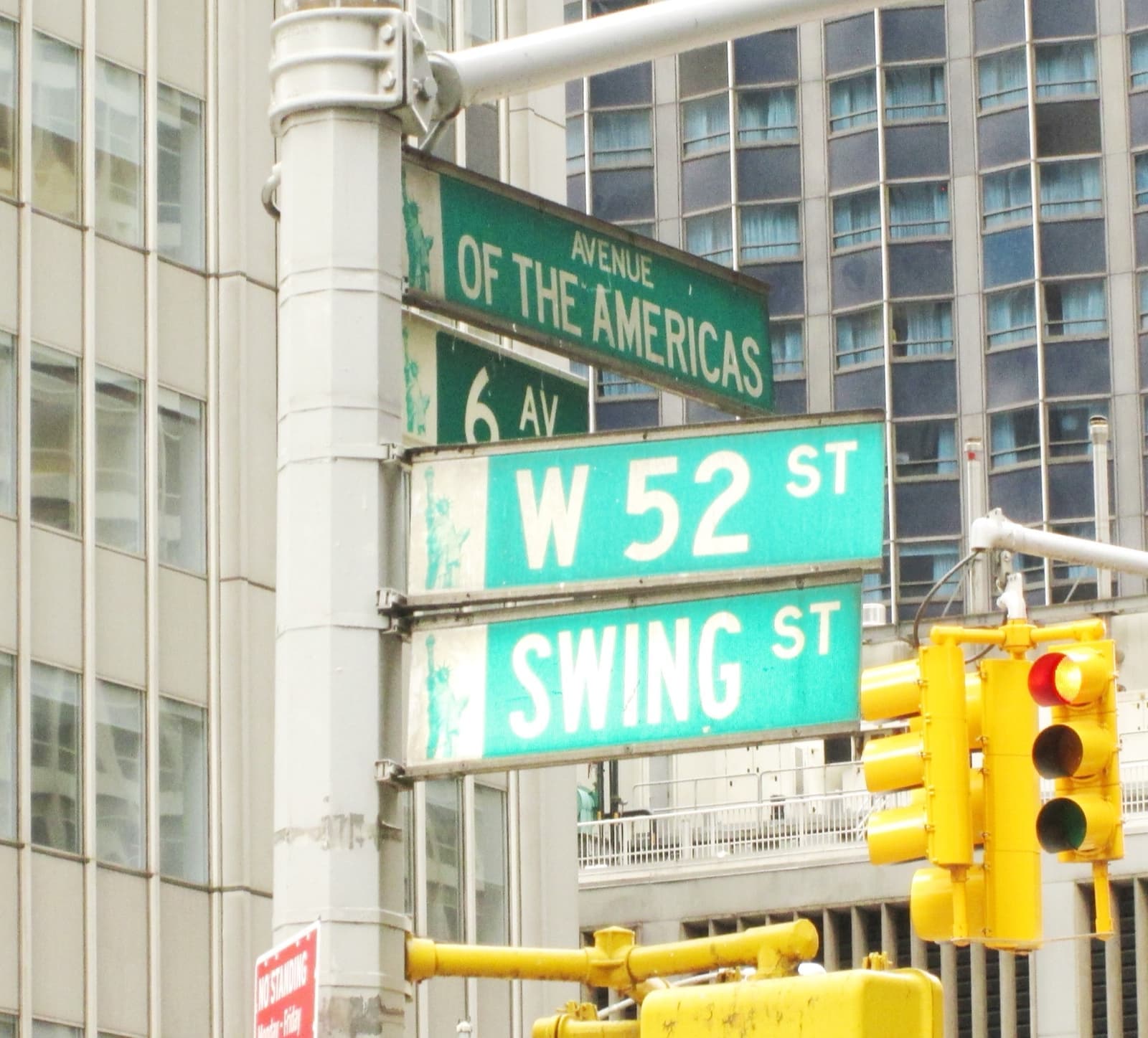 Green street signs for W 52 St and Swing St on a pole at Sixth Avenue, office towers behind