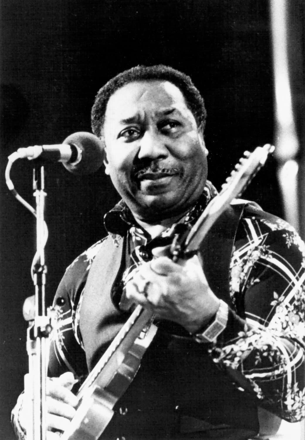 Muddy Waters at a microphone with an electric guitar, smiling sideways
