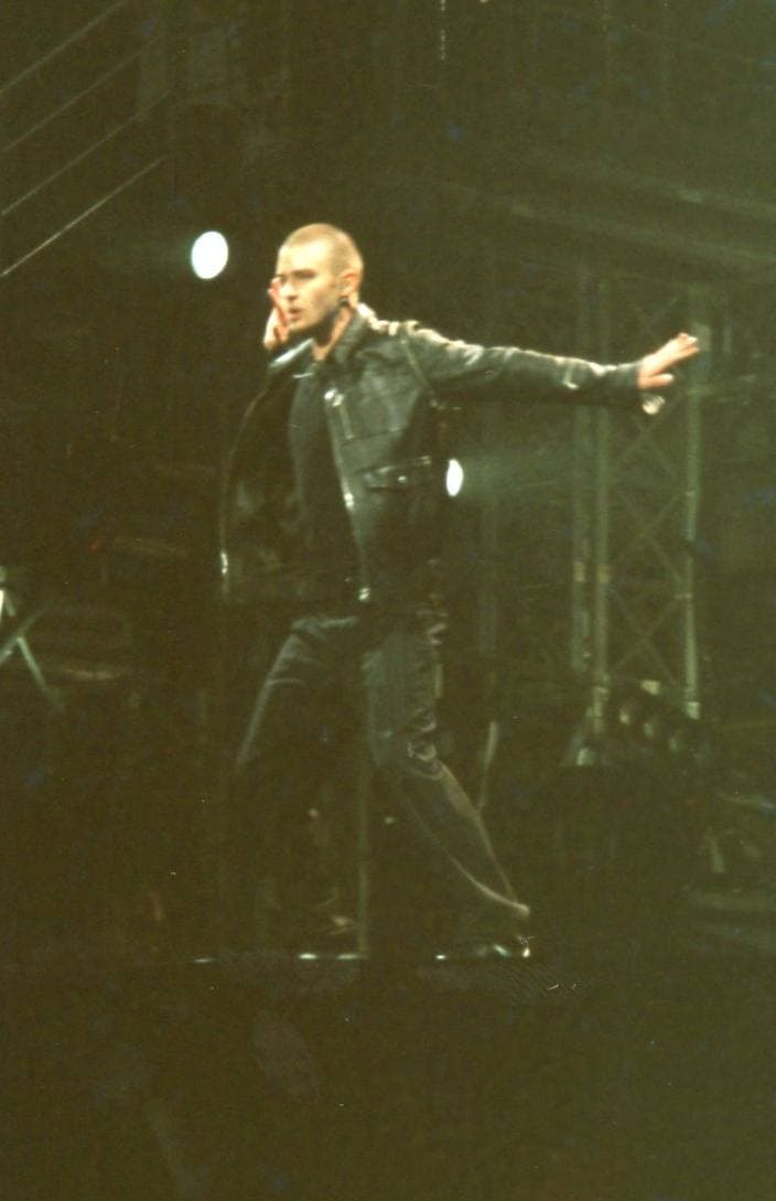 A singer in a white shirt performing on a lit stage