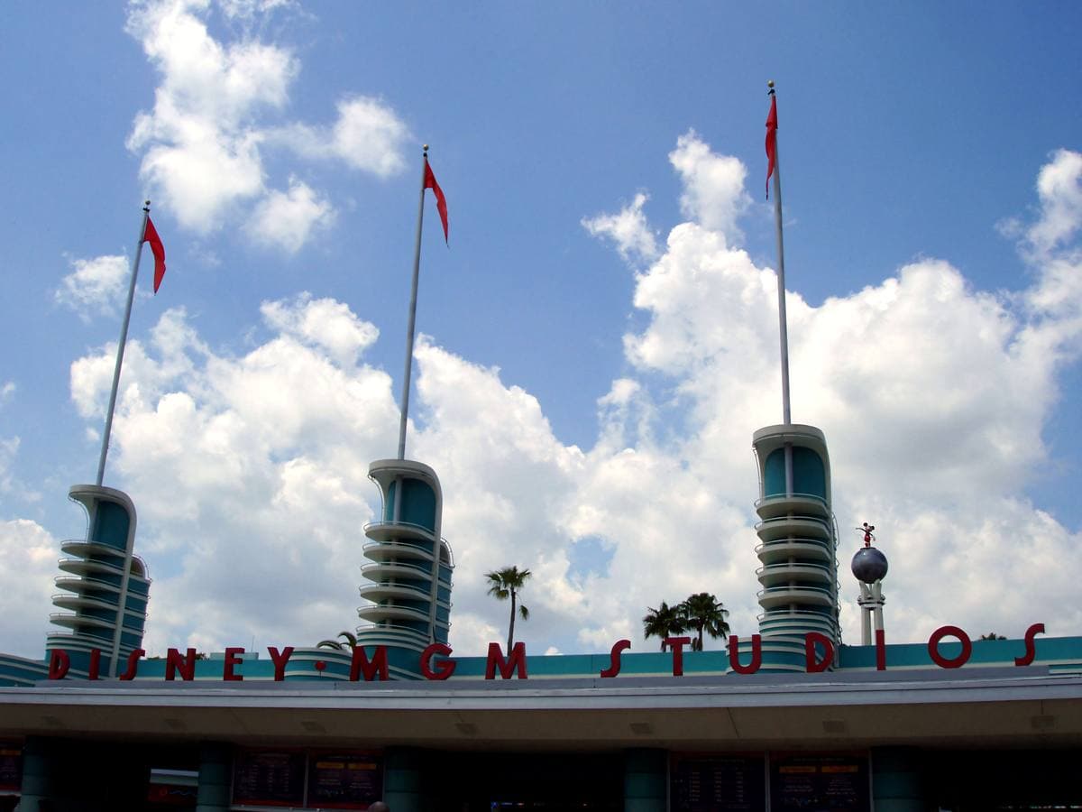 A theme park entrance sign with three towers and red pennants