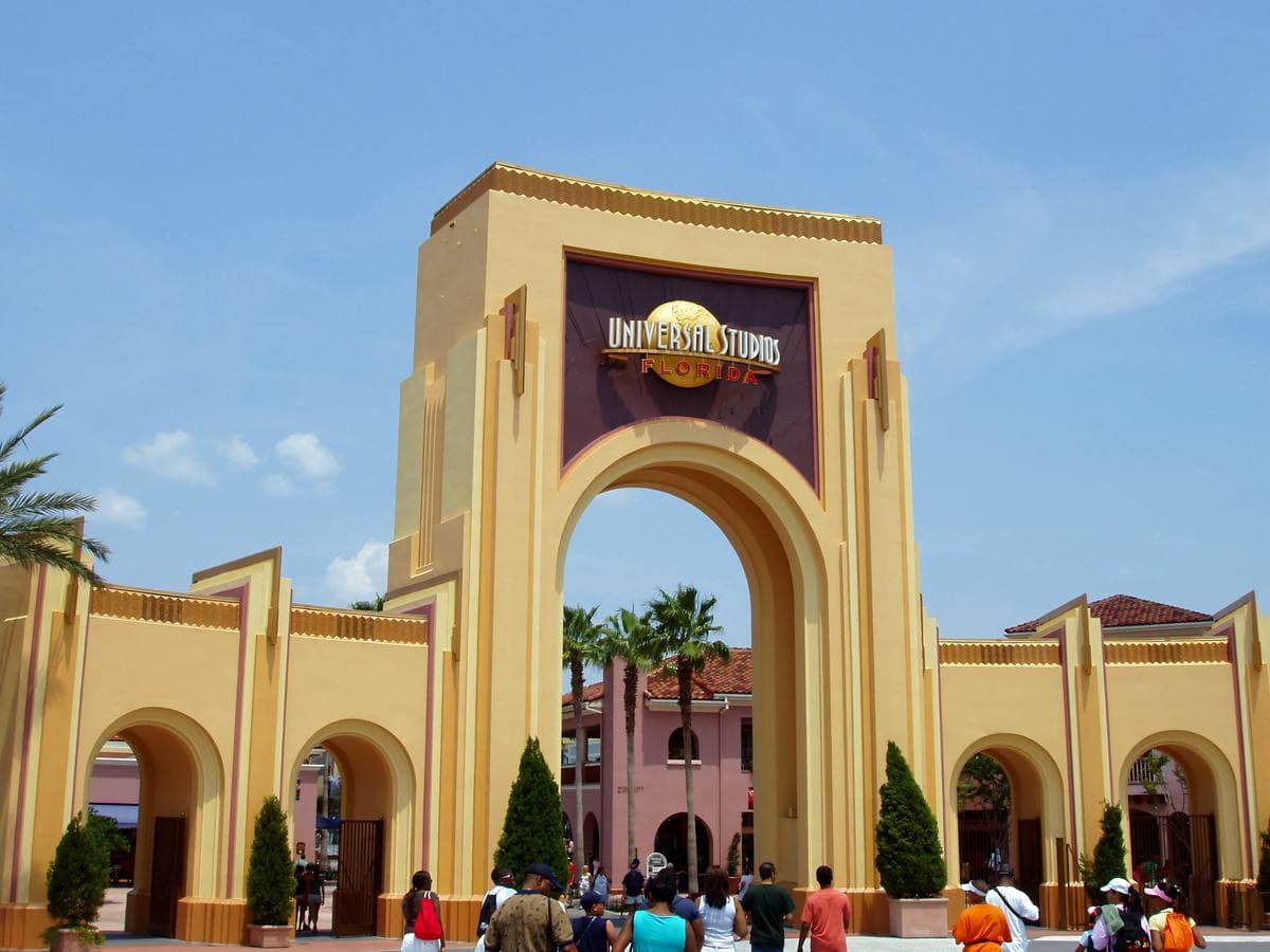 A theme park entrance arch over turnstiles under a blue sky