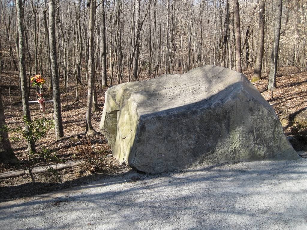 A large engraved boulder beside a gravel path among bare winter trees